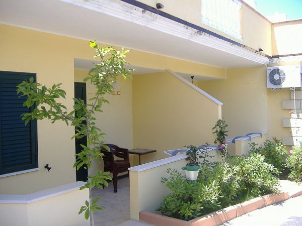 Ingresso di una casa color crema con piante verdi e una piccola veranda.