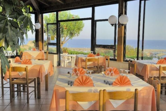 Ristorante con tavoli apparecchiati vicino a finestre, vista sul mare e giardino.