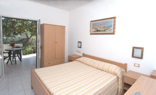 Stanza da letto con letto matrimoniale, armadio in legno, e porta aperta verso un balcone.