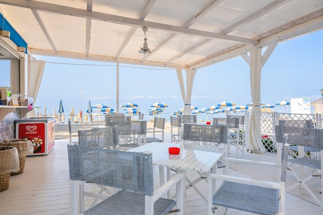 Terrazza con tavoli, sedie e vista mare e ombrelloni.