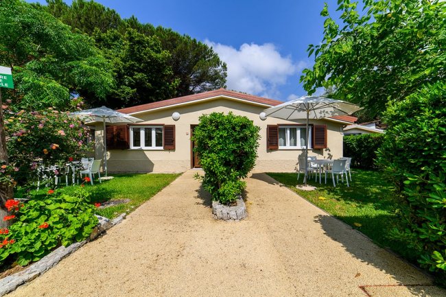 Casetta gialla con giardino fiorito e ombrelloni.