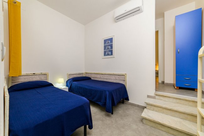 Camera con due letti singoli blu e scale.