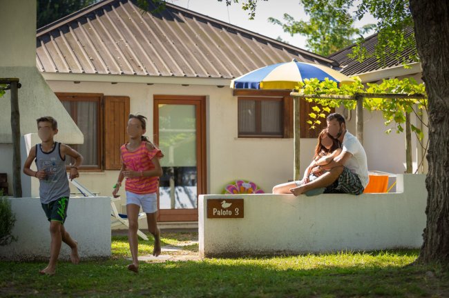 Due bambini corrono vicino a un bungalow, coppia seduta sul muretto.