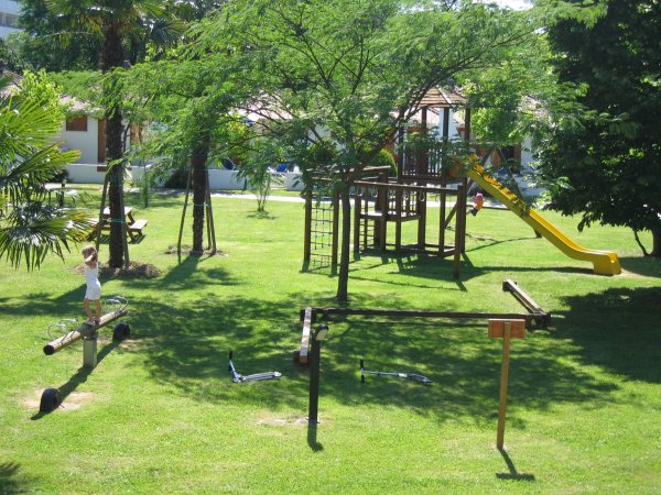 Parco giochi su prato verde con scivolo e altalene.