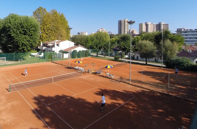 Campi da tennis all'aperto con giocatori e ombrelloni.