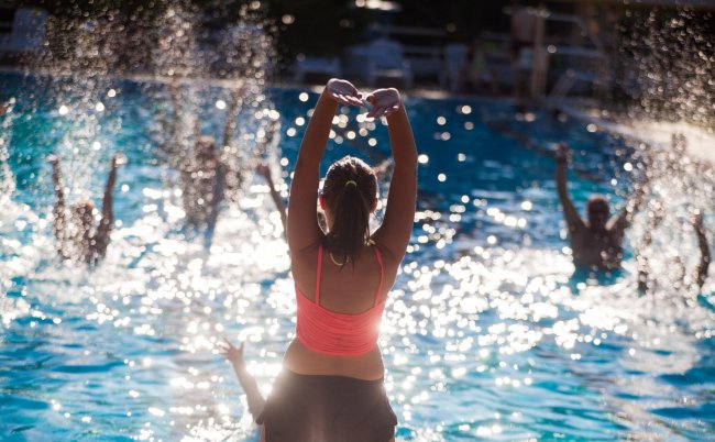 Persone fanno acquagym in piscina, molta luce e schizzi d'acqua.