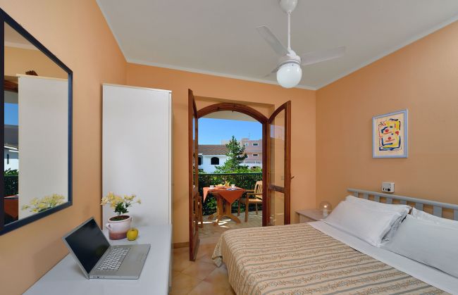 Una camera da letto con balcone, letto matrimoniale e ventilatore a soffitto.