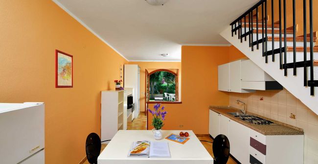 Cucina arancione con tavolo bianco e scala laterale.