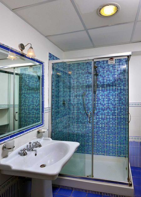 Bagno con box doccia a mosaico blu e lavabo bianco.