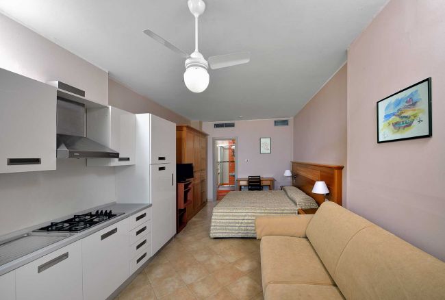 Camera con cucina, letto e divano beige.