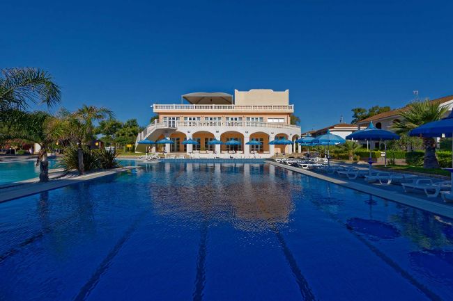 Edificio coloniale con piscina e ombrelloni blu.
