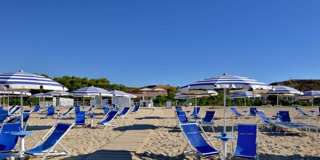 Lettini e ombrelloni blu su spiaggia soleggiata.
