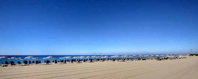 Lunga spiaggia con file di sedie e ombrelloni.