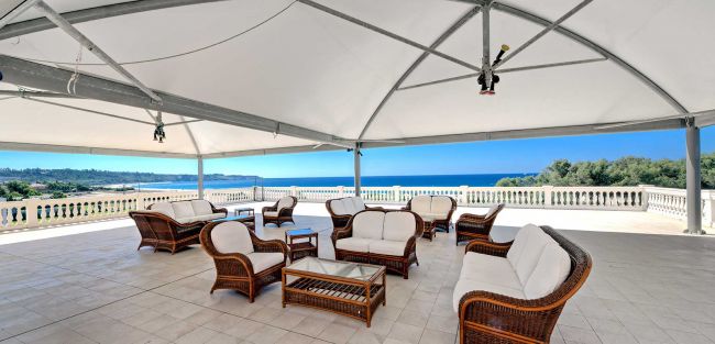 Un patio coperto con mobili in vimini e vista mare.