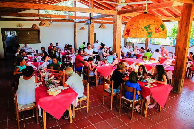 Persone sedute a tavoli con tovaglie rosse in un ristorante coperto con travi di legno.