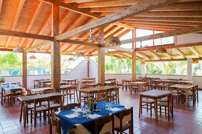Ristorante con tavoli apparecchiati, soffitto in legno e ampie finestre.