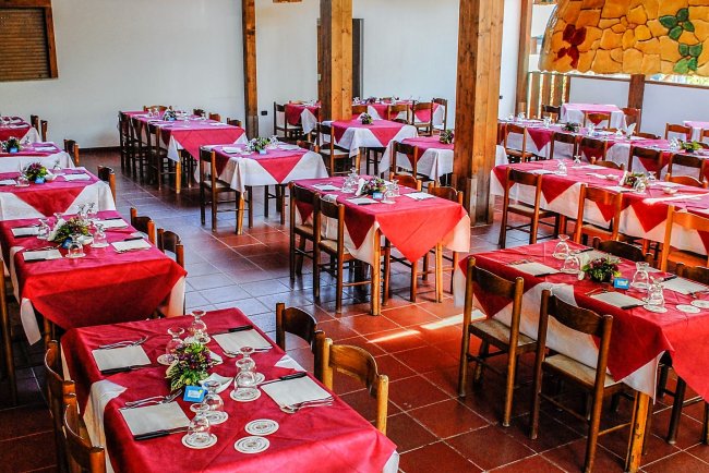 Sala ristorante con tavoli apparecchiati con tovaglie rosse e decorazioni floreali.