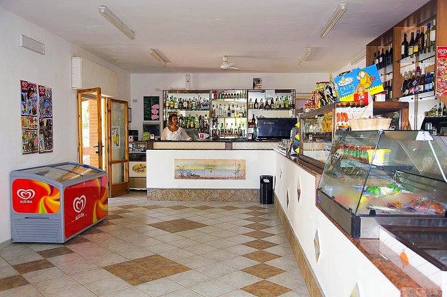 Interno di un bar con bancone fornito di bevande e un congelatore Algida.