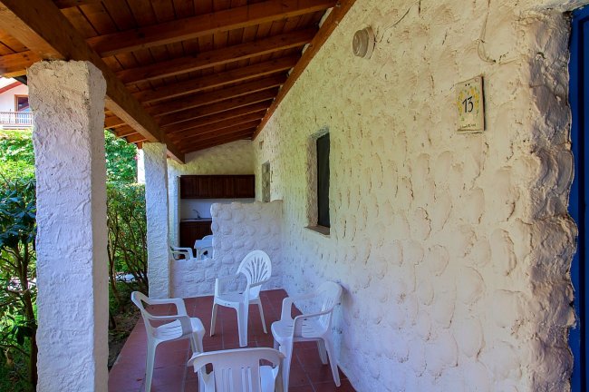 Portico in pietra bianca con sedie di plastica sotto un tetto di legno.