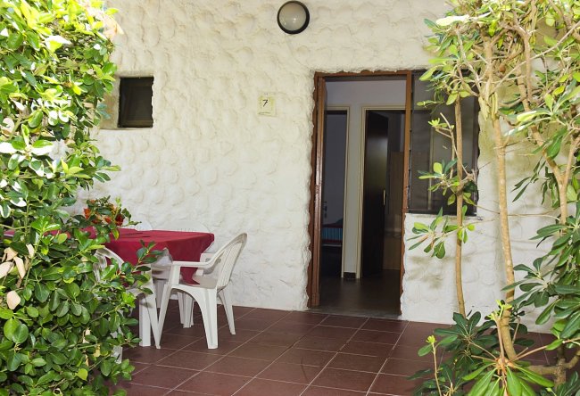 Una veranda con tavolo e sedie bianche, circondata da piante verdi.