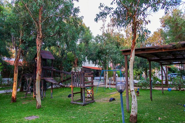 Area giochi all'aperto con strutture in legno tra alberi e prato.