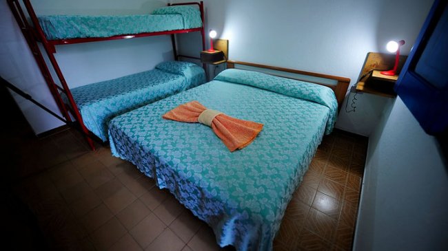 Letto matrimoniale con copriletto azzurro e letto a castello, lampade accese sui comodini.