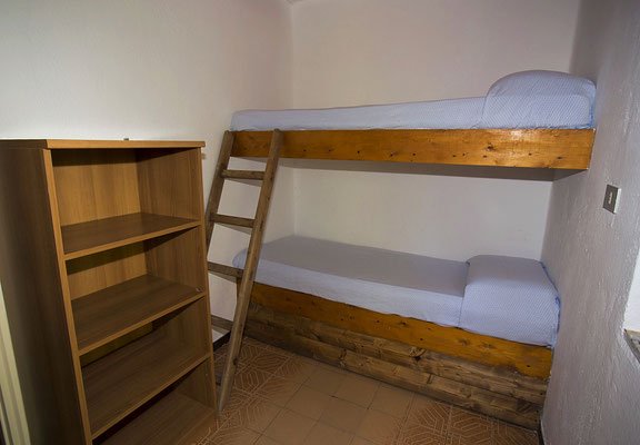 Letto a castello in legno con scala, accanto a una libreria vuota in una stanza.