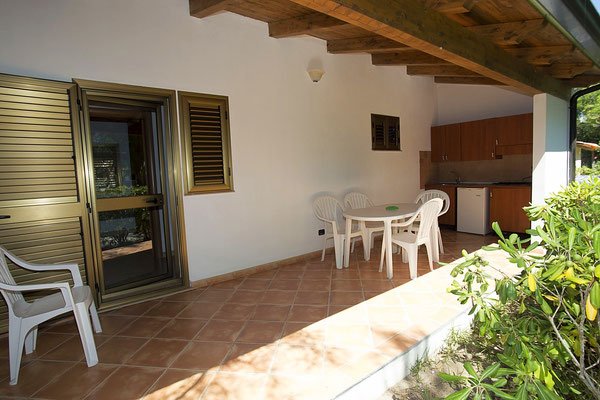 Veranda con tavolo e sedie in plastica, affacciata su un giardino, con angolo cottura.