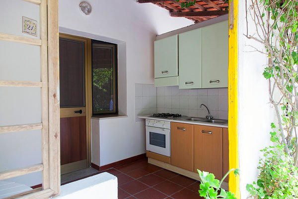 Cucina all'aperto con forno, fornelli, lavello e armadietto, vicino a una porta finestra.