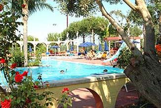 Una piscina circondata da alberi e fiori con persone che nuotano e prendono il sole.