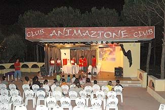 Spettacolo serale in un anfiteatro con sedie bianche e palco con tenda, scritto 