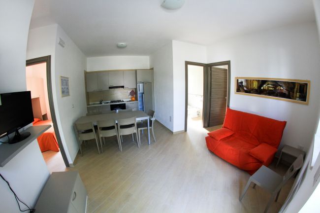 Soggiorno con cucina, tavolo, e divano rosso.