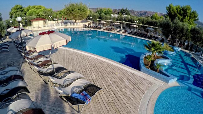 Piscina circondata da lettini e ombrelloni su una terrazza in legno.