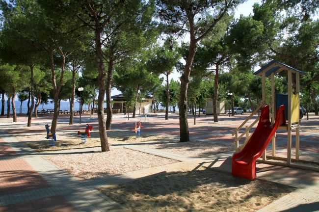 Parco giochi tra gli alberi con scivolo rosso e giochi a molla.