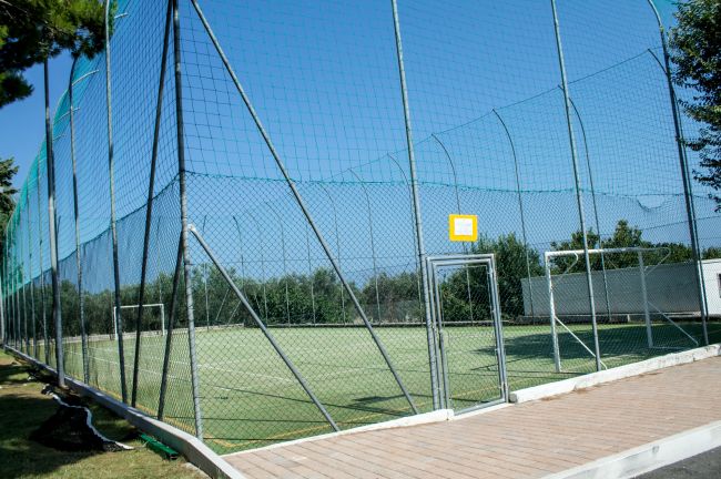Campo da calcio recintato, con rete alta e cancello d'ingresso.