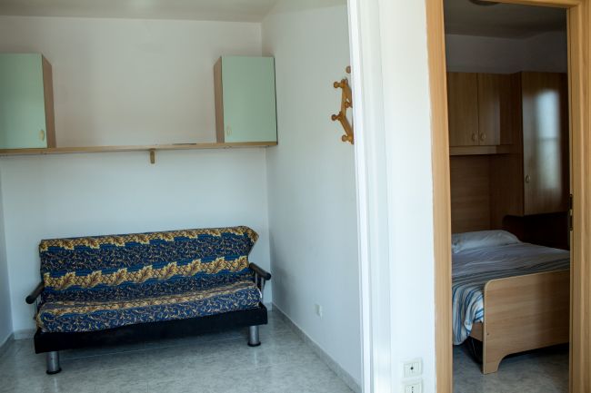 Soggiorno con divano blu e camera da letto adiacente.