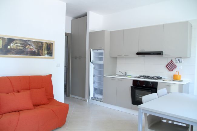 Soggiorno con divano arancione e cucina grigia.