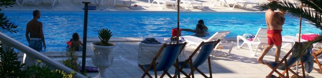 Persone in piscina con sdraio e piante attorno.