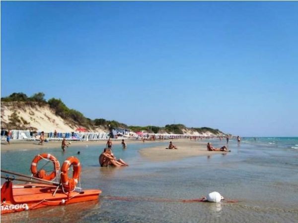 Spiaggia affollata con persone che si rilassano vicino all'acqua, bandiera di salvataggio visibile.