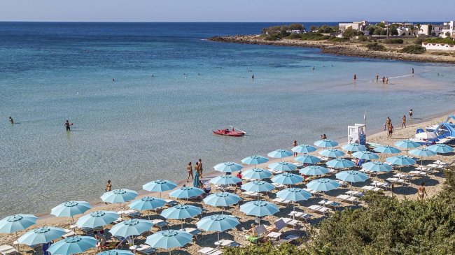 Spiaggia con ombrelloni azzurri e mare calmo.