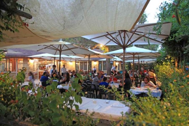 Ristorante all'aperto affollato, tavoli sotto ombrelloni.