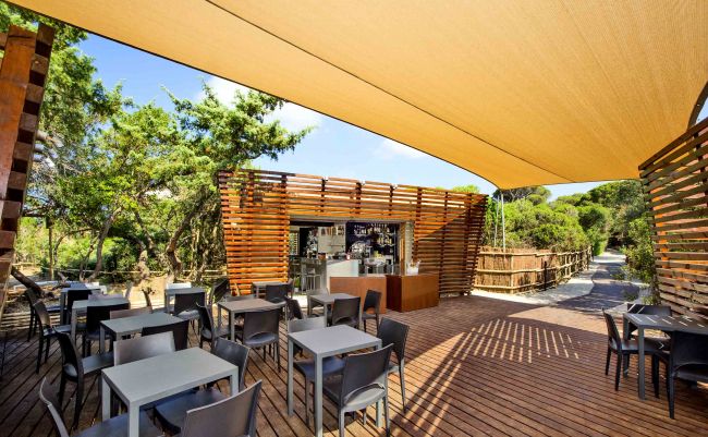 Terrazza con tavoli, sedie e bar. Ombrellone beige sopra.