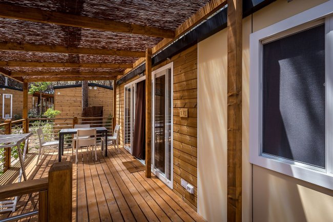 Veranda in legno coperta con tavolo e sedie di fronte a un bungalow.