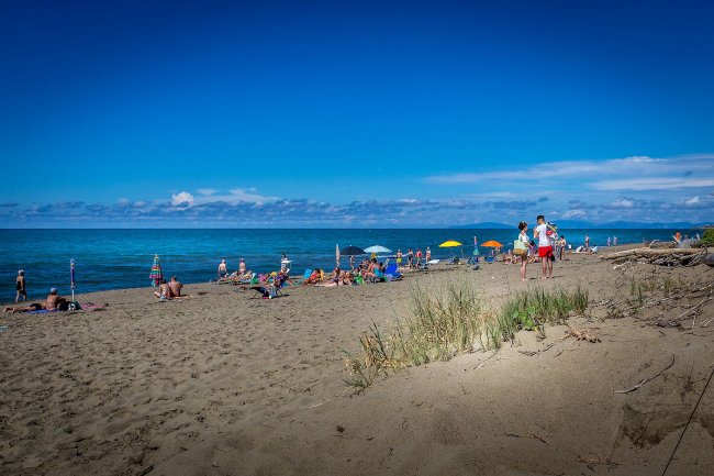 Spiaggia affollata con bagnanti e ombrelloni colorati.