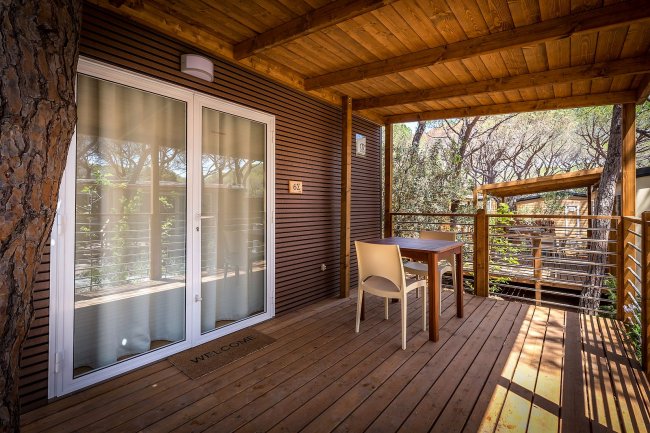 Terrazza in legno con tavolo e sedie all'ingresso di una casa nel bosco.