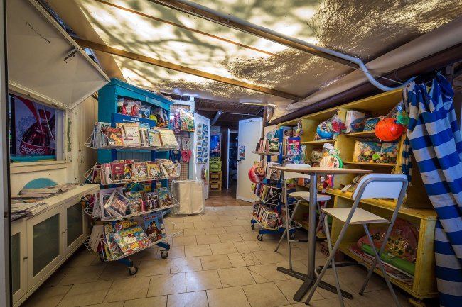 Un negozio con scaffali pieni di riviste, giochi gonfiabili e souvenir colorati.