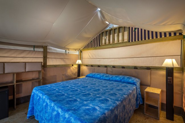 Interno di una tenda con letto matrimoniale e illuminazione soffusa.