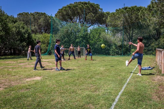 Gruppo di ragazzi gioca a calcio su un campo erboso con reti verdi.