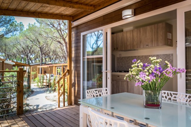 Tavolo con sedie e vaso di fiori su una terrazza, all'esterno di un bungalow immerso nella natura.