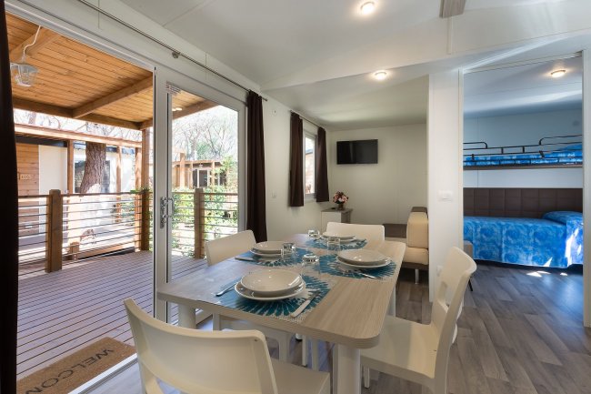 Interno di una casa moderna con tavolo da pranzo apparecchiato e camera da letto sullo sfondo.